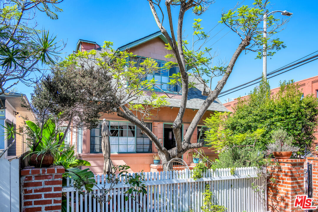 Peach two-story home behind a white picket fence and leafy trees.