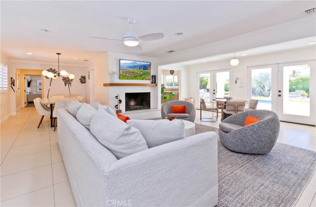 Furnished living room with a fireplace, gray seating, and glass doors overlooking a pool.