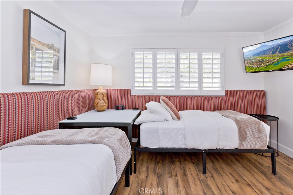 Bedroom with two beds, a red patterned headboard, plantation shutters, and wood-look flooring.