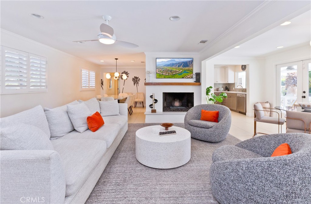 Staged living room with a fireplace, white sofa, gray chairs, and orange accent pillows.