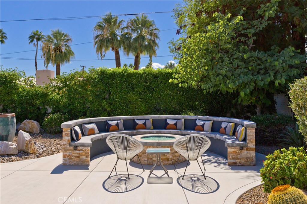 Furnished patio with a curved stone bench, patterned cushions, and two wire chairs.