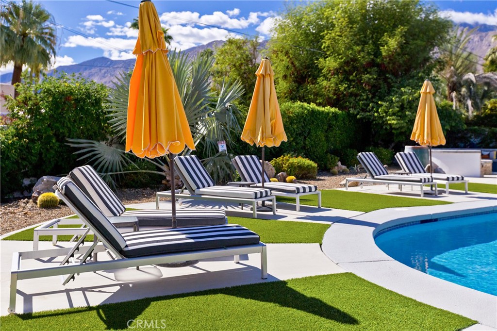 Palm Springs poolside with striped chaise lounges, orange umbrellas, and mountain views.