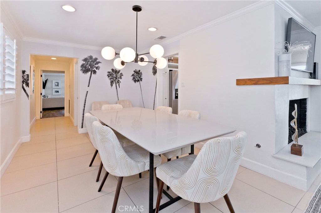 Dining room with a long white table, patterned chairs, palm tree mural, and globe chandelier.