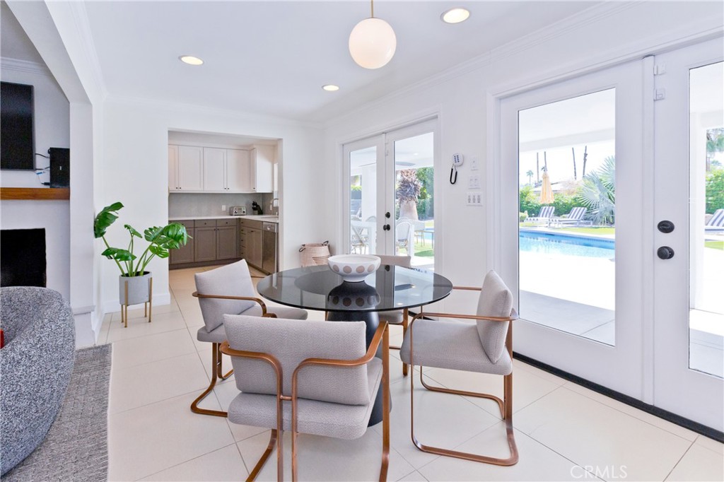 Dining area with a round glass table and chairs, opening to a kitchen and poolside patio.