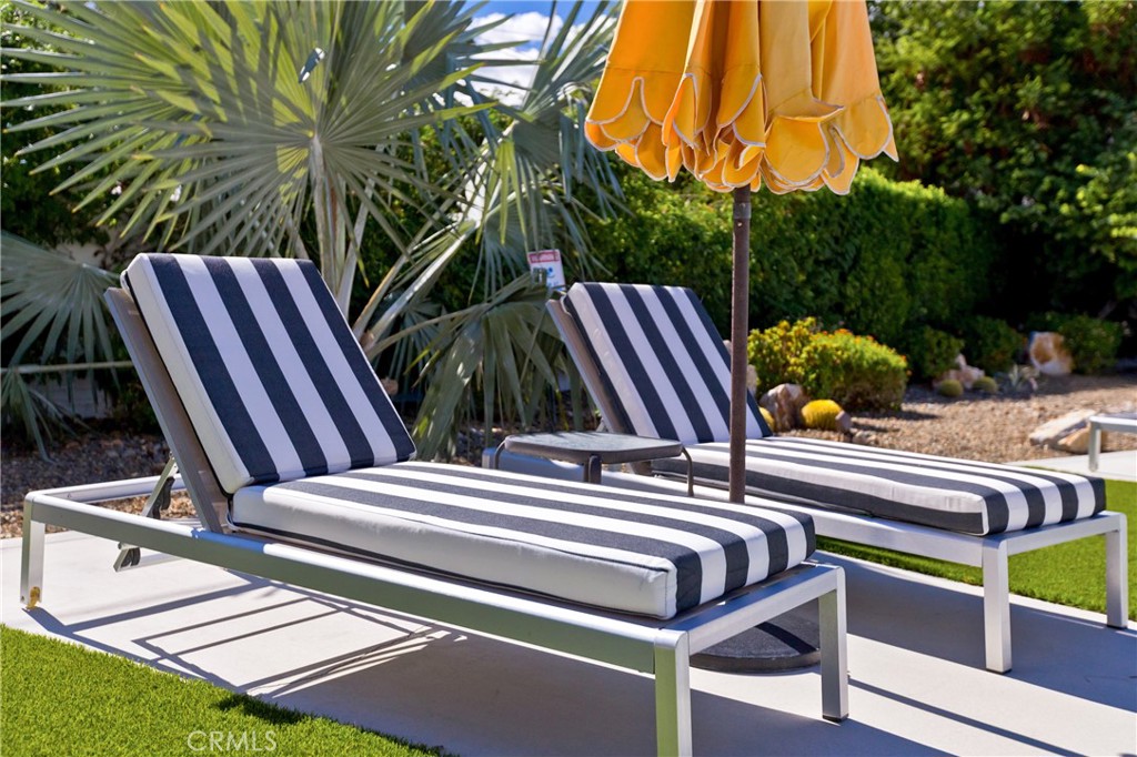 Two striped chaise lounges and an orange umbrella on a landscaped patio.
