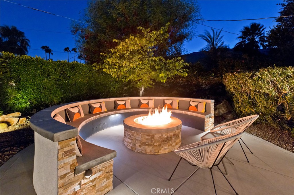 Outdoor patio with a glowing fire pit, curved built-in seating, and two woven chairs at night.