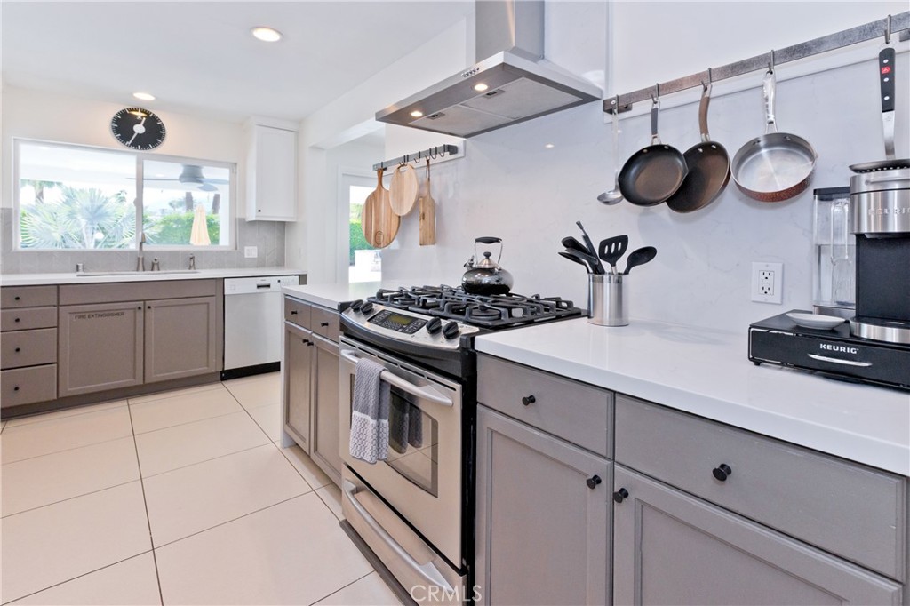 Kitchen with taupe cabinets, white counters, stainless steel gas range, and hanging pans.