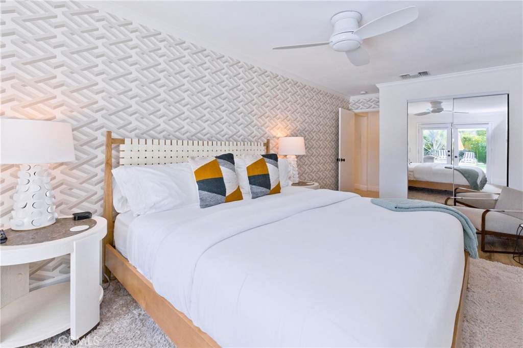 Bedroom with a white bed, geometric wallpaper, colorful accent pillows, and mirrored closet doors.