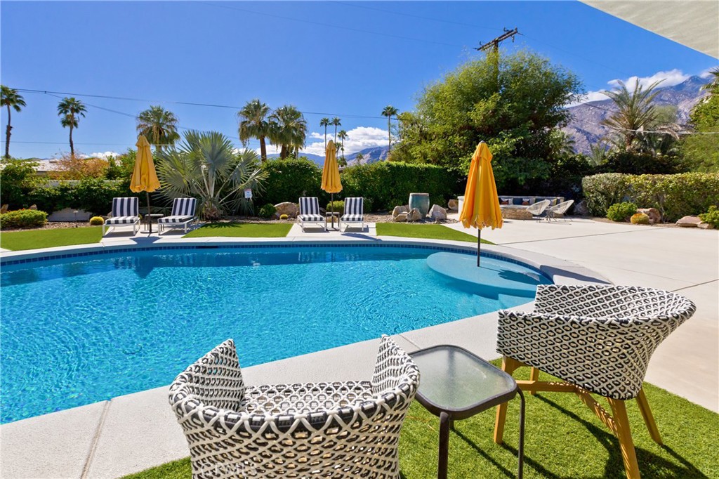 Backyard pool with yellow umbrellas, patterned lounge chairs, and mountains beyond the garden.