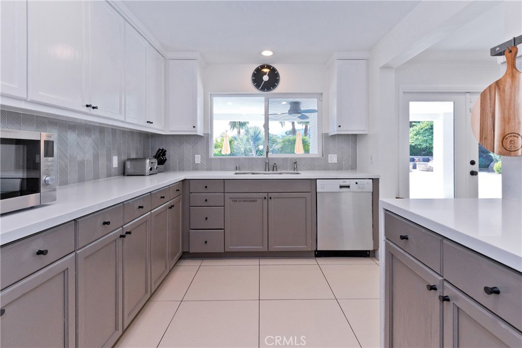 Kitchen with gray cabinetry, herringbone backsplash, and a window overlooking palms.