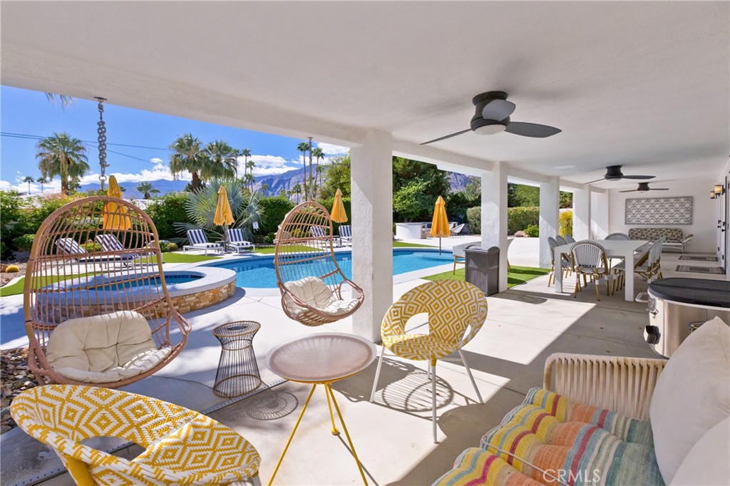Covered patio with hanging chairs and dining area overlooking a pool and mountain views.