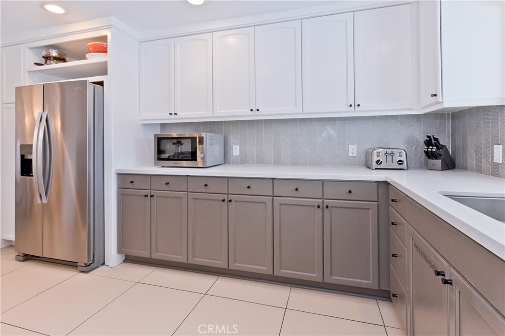 Modern kitchen with white and taupe cabinets, gray herringbone backsplash, and stainless-steel refrigerator.