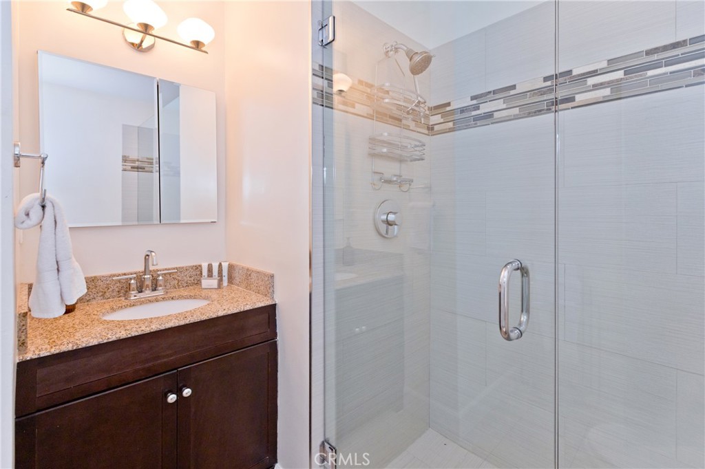 Bathroom with granite vanity and glass-enclosed tiled shower.