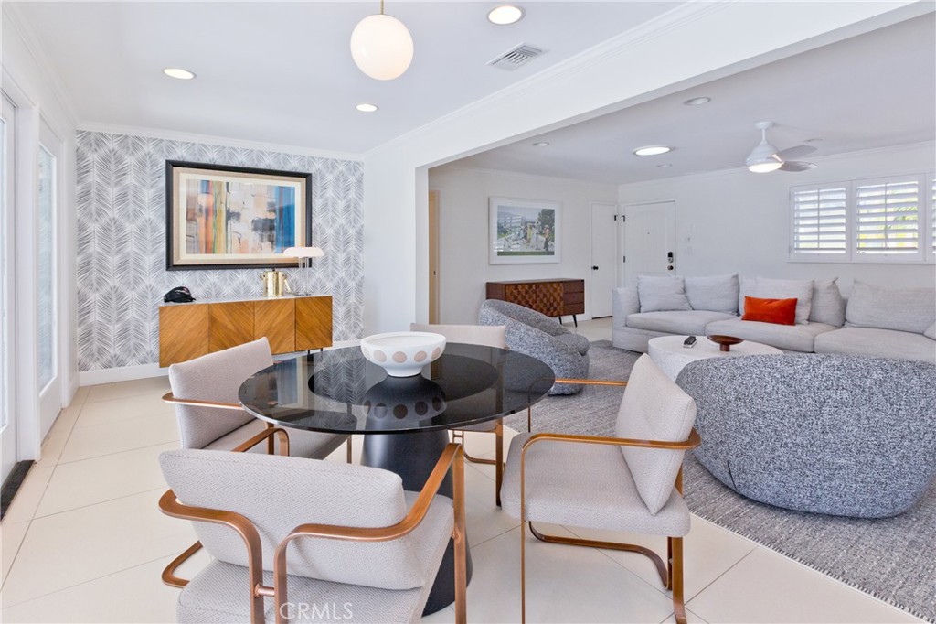 Open-plan living and dining room with a glass table, gray sectional, and patterned accent wall.