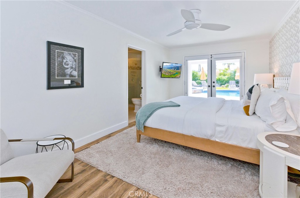 Bright bedroom with a king bed, teal throw, and glass doors opening toward a swimming pool.