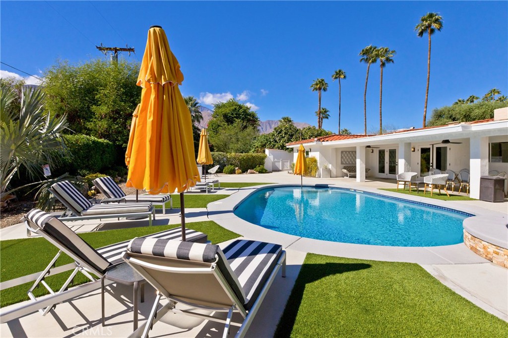 Backyard pool with striped loungers and yellow umbrellas, framed by palm trees and distant mountains.