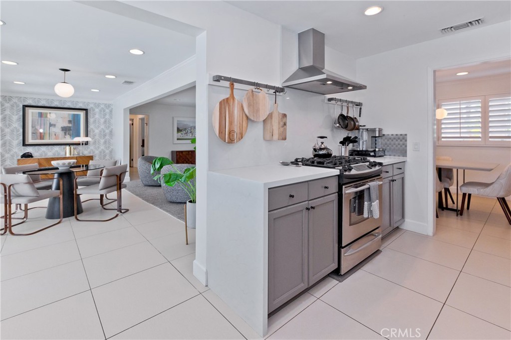 Staged kitchen with gray cabinets and stainless range opening to a dining area.