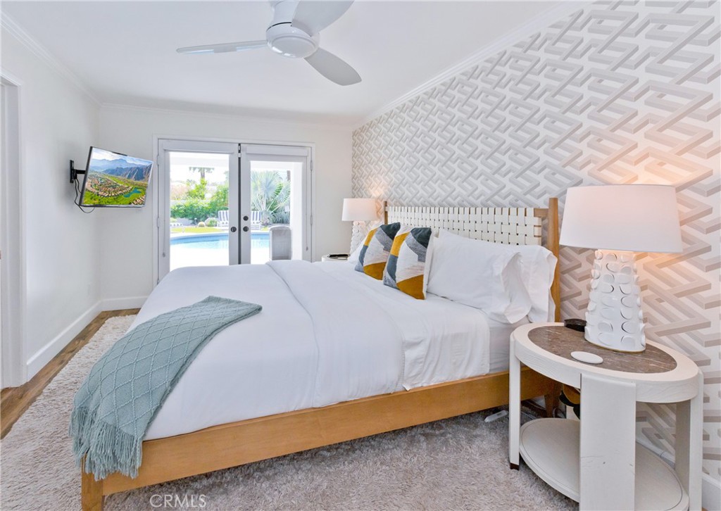 Bedroom with geometric wallpaper, a wood-framed bed, and French doors overlooking the pool.