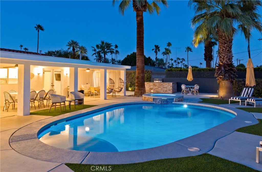Backyard pool and covered patio with palms at dusk.