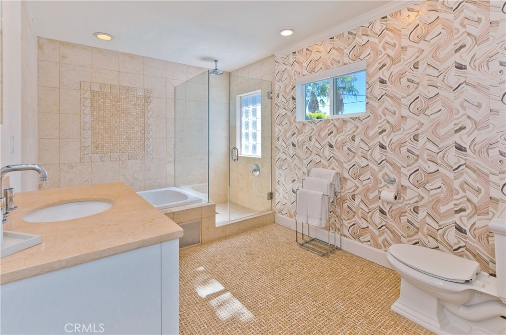 Bathroom with a glass-enclosed shower, stone vanity, and bold patterned wallpaper.