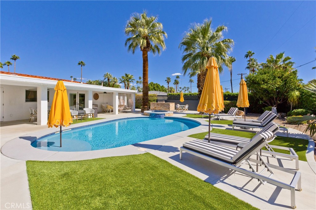 Palm Springs pool with a raised spa, striped loungers, yellow umbrellas, and tall palm trees.