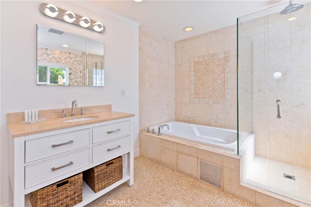 Bathroom with a white vanity, tiled bathtub, and glass-enclosed shower.