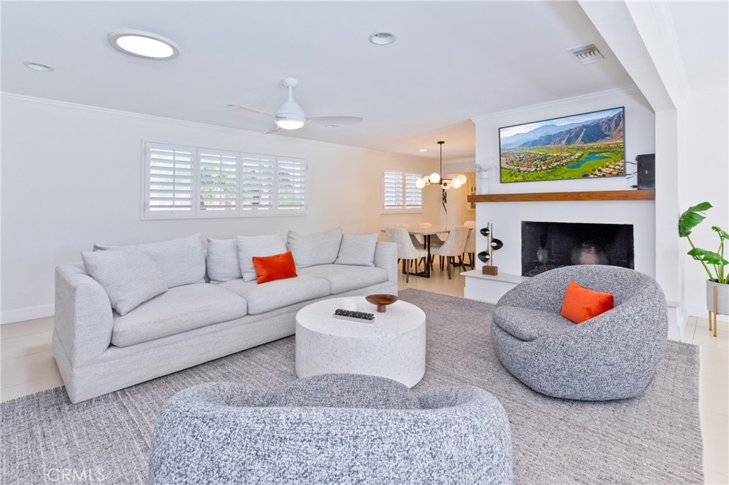 Staged living room with gray seating, plantation shutters, and a fireplace with a wood mantel.
