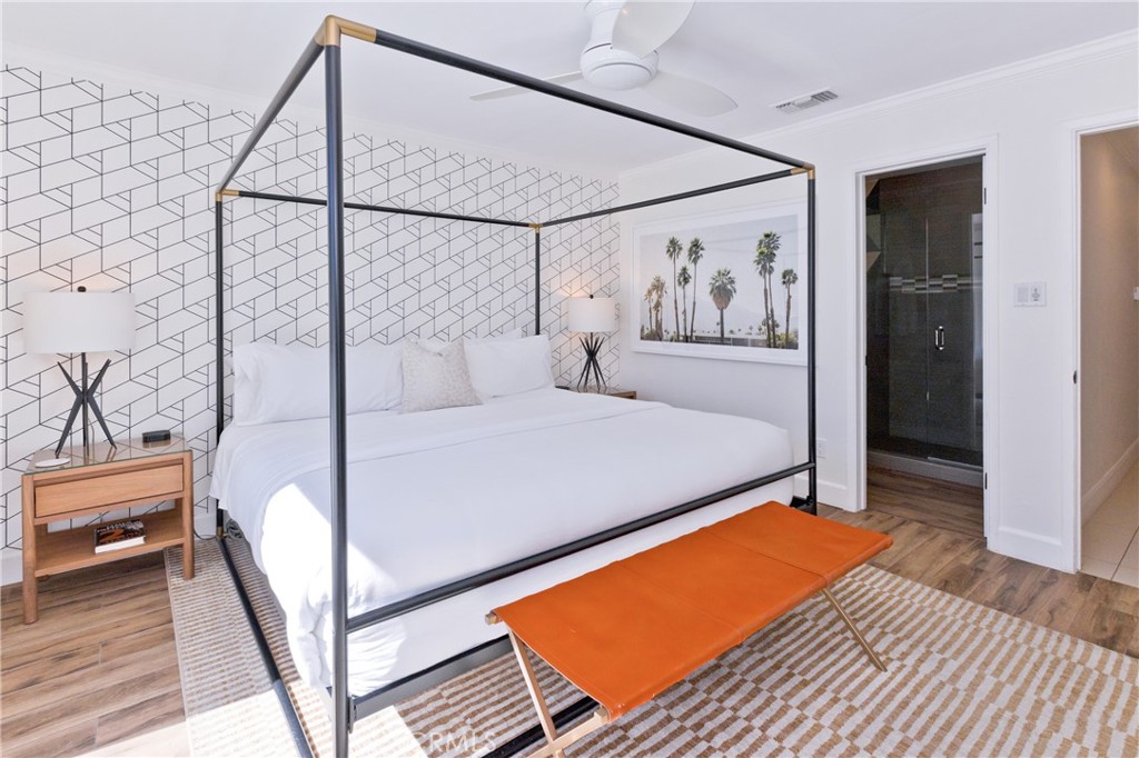 Bedroom with a white canopy bed, geometric accent wall, palm tree artwork, and orange bench.