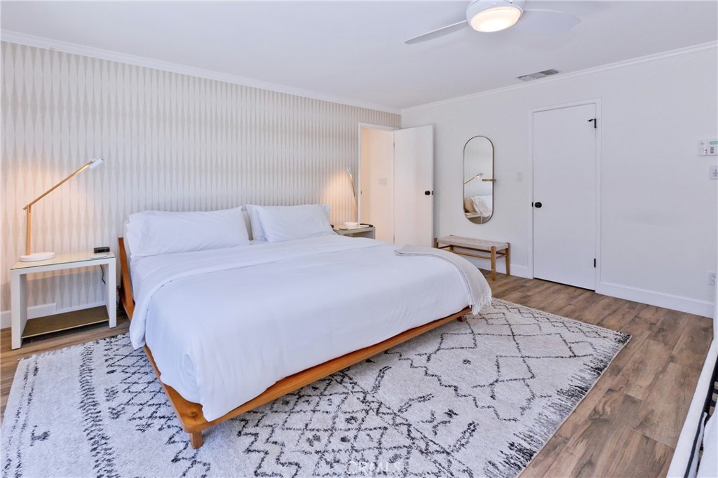 Bedroom with a low wooden bed, white linens, patterned wallpaper, and a geometric rug.