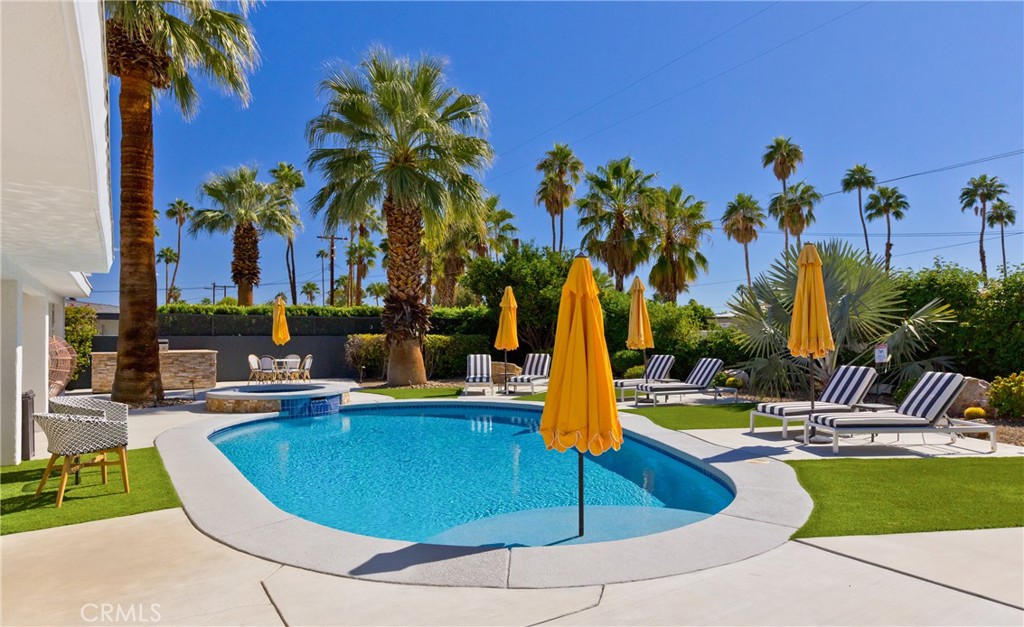 Backyard pool with yellow umbrellas, striped loungers, artificial turf, and palm trees.