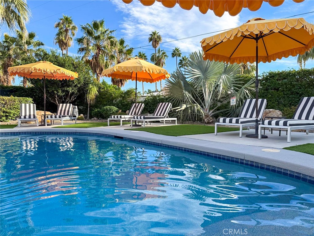 Swimming pool bordered by striped loungers and orange umbrellas among palm trees.