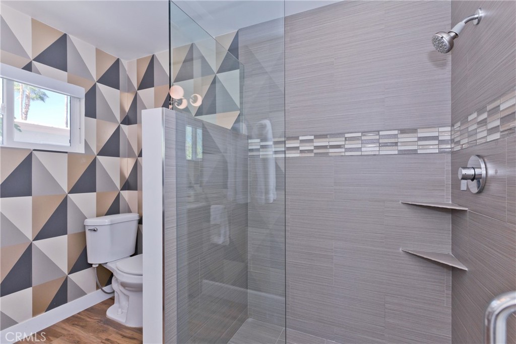 Bathroom with a glass-enclosed gray-tile shower and bold geometric tile behind the toilet.