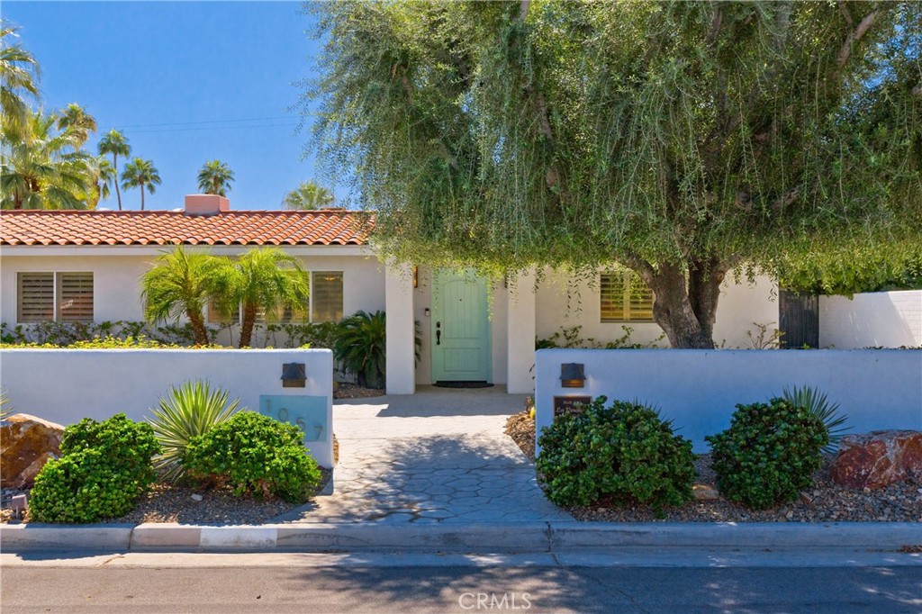 White single-story home with a turquoise entry door, terracotta tile roof, and shady landscaped front walkway.