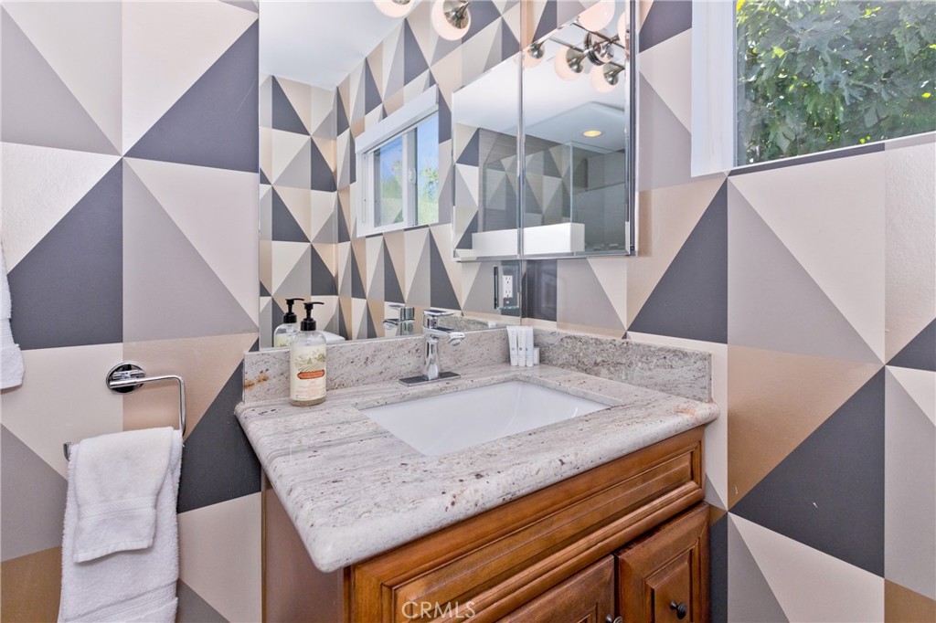 Bathroom vanity with a marbled countertop, wood cabinetry, and bold geometric wall tiles.