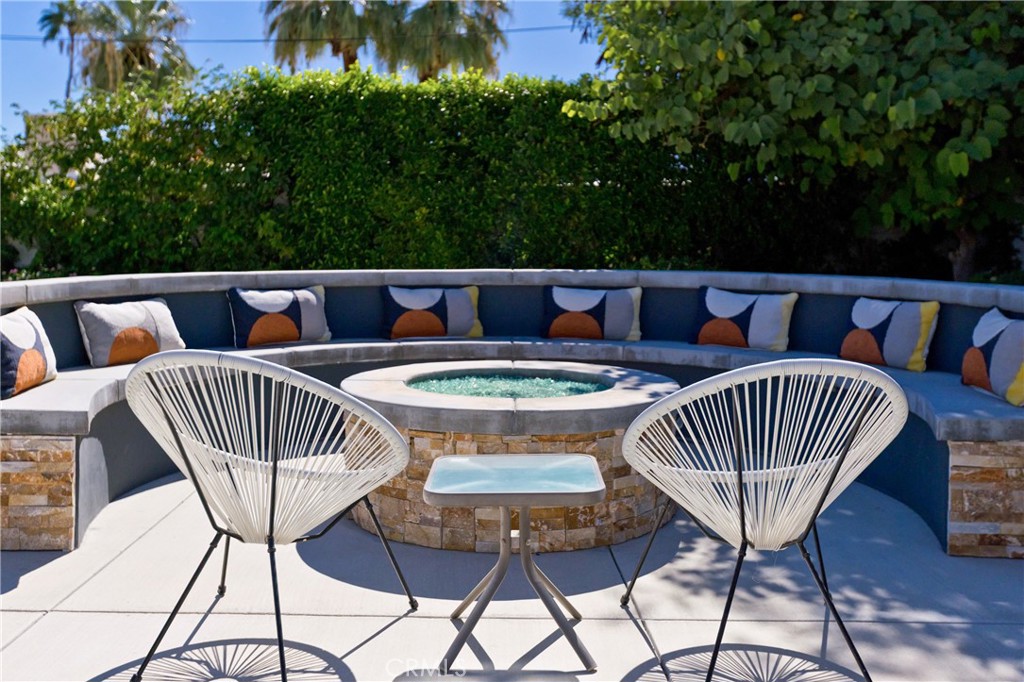 Raised circular spa surrounded by curved blue seating and white woven chairs on a sunny patio.