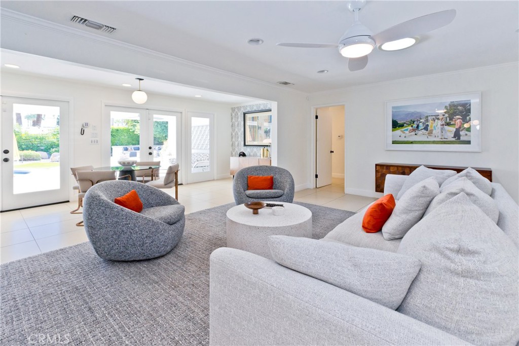 Staged living room with a gray sectional, orange-accented armchairs, and glass doors opening to greenery.