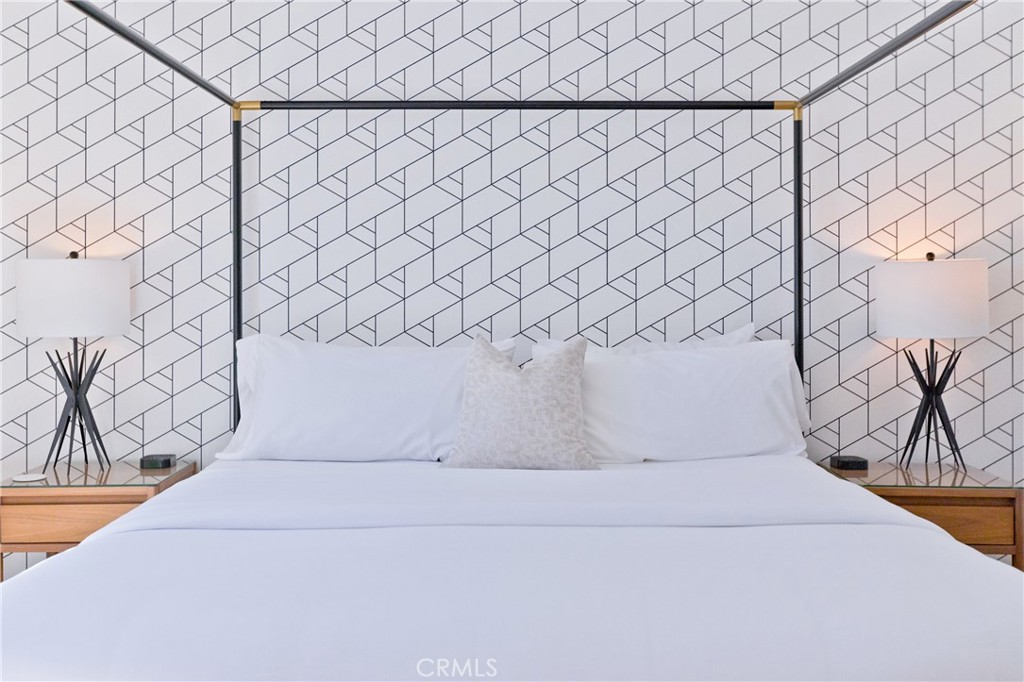 Bedroom with a white bed, geometric wallpaper, black metal headboard, and matching bedside lamps.