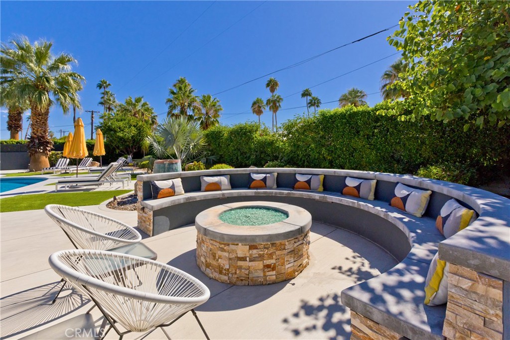 Palm Springs backyard patio with curved cushioned seating, a round fire feature, and swimming pool.