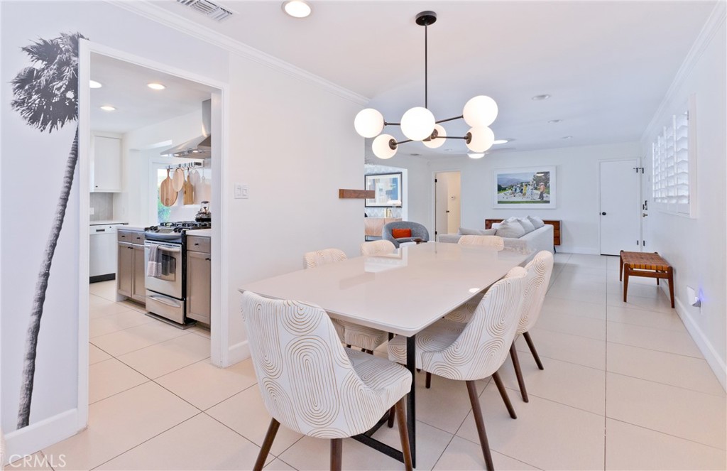 Dining area with a large white table, patterned chairs, and an adjoining kitchen and living room.