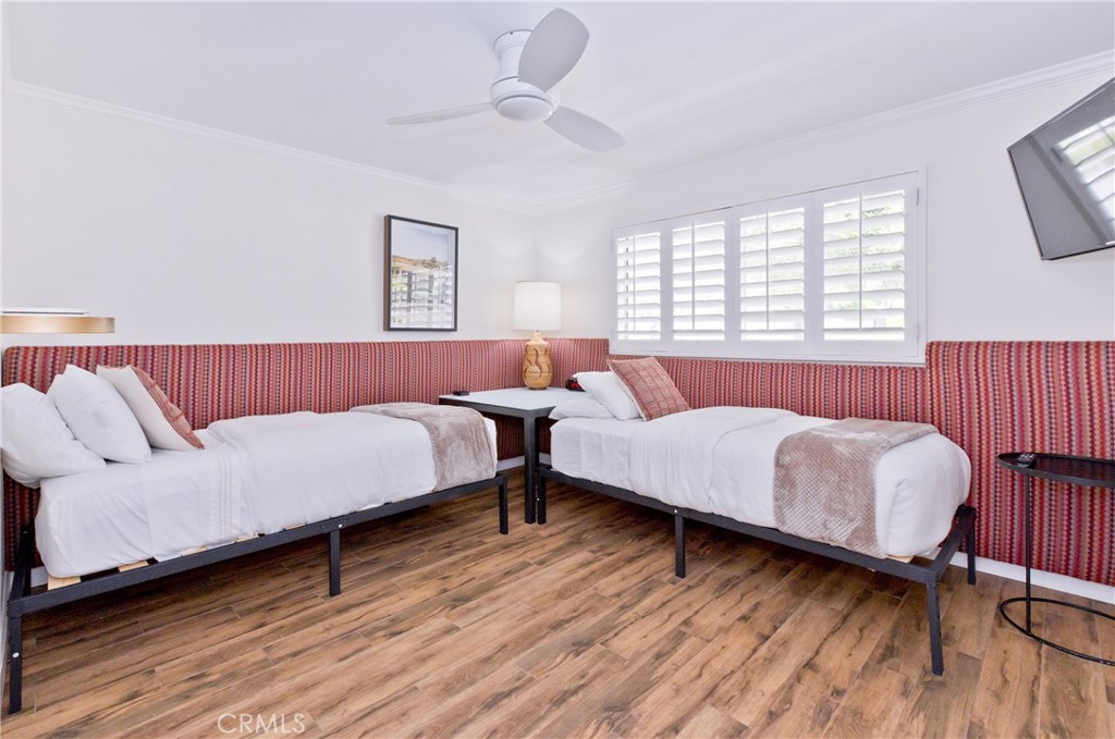 Bedroom with two twin beds, red patterned wall upholstery, and white plantation shutters.
