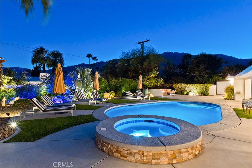 Backyard pool and raised circular spa at dusk, with lounge chairs and mountains in the background.