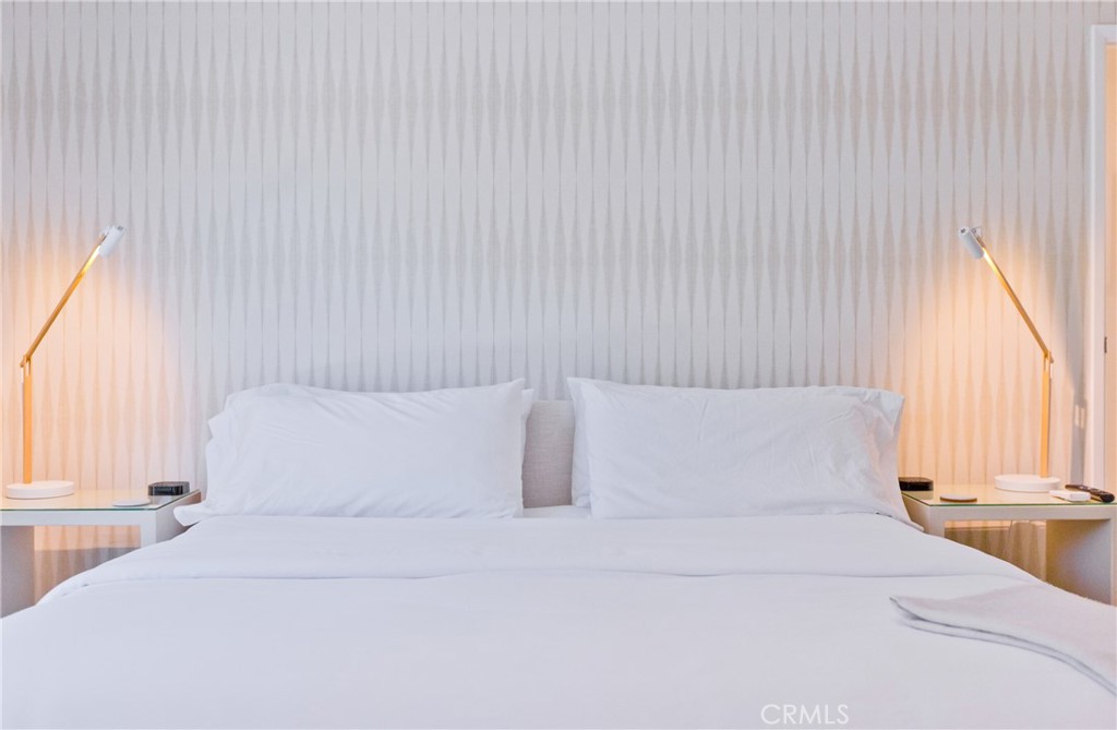 White bed with matching brass bedside lamps and a tall patterned headboard.