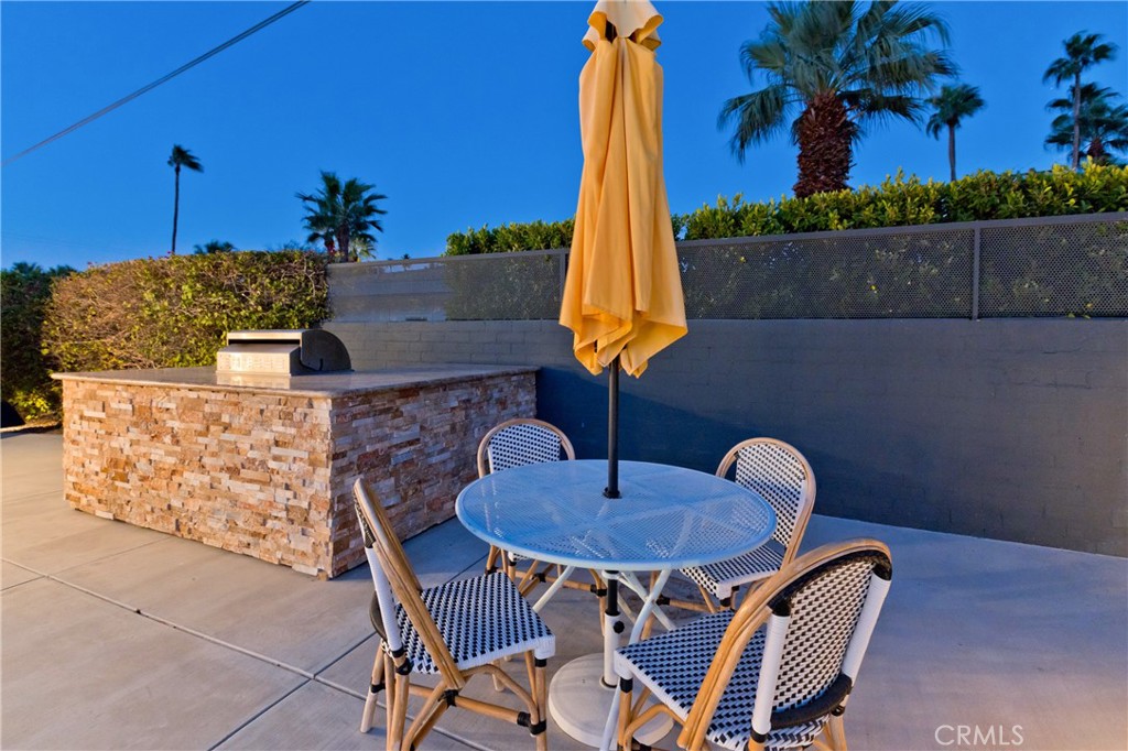 Patio dining area with a yellow umbrella, woven chairs, and a stone counter with built-in grill.