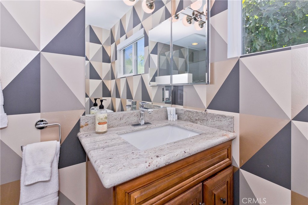 Bathroom vanity with geometric tile, granite countertop, wood cabinetry, and mirrored medicine cabinet.