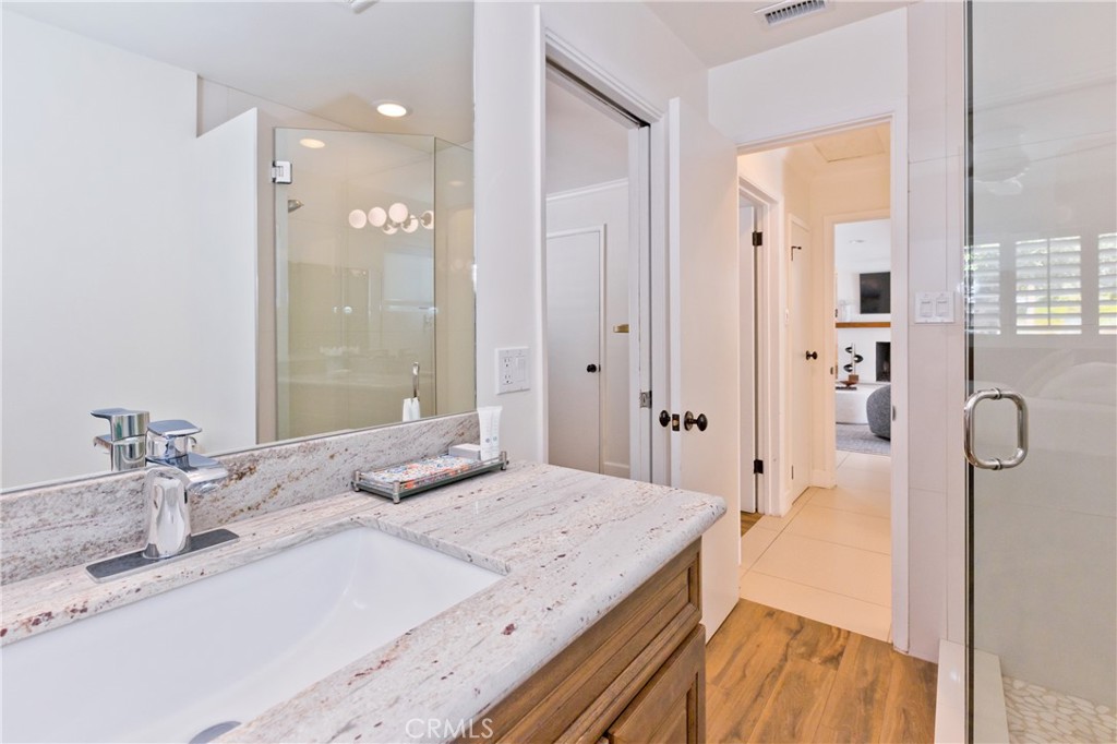 Bathroom with a speckled stone vanity, glass shower enclosure, and wood-look flooring.