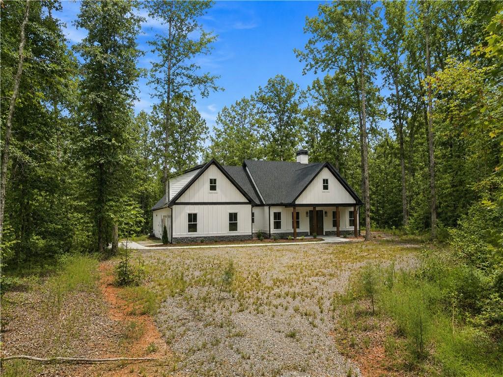 White-sided home with a dark gabled roof and gravel driveway, surrounded by trees.