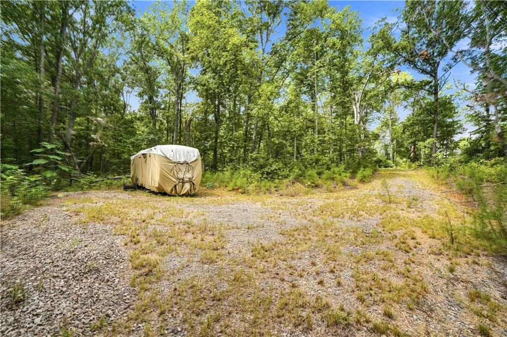 Wooded property with a broad gravel clearing and a tarp-covered object near the trees.