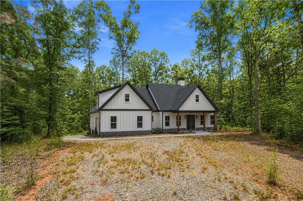 White farmhouse with dark gabled roofs, surrounded by trees beside a gravel driveway.