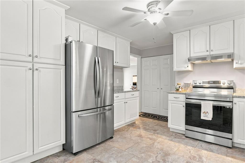 White kitchen with stainless steel refrigerator, range, and stone-look tile flooring.