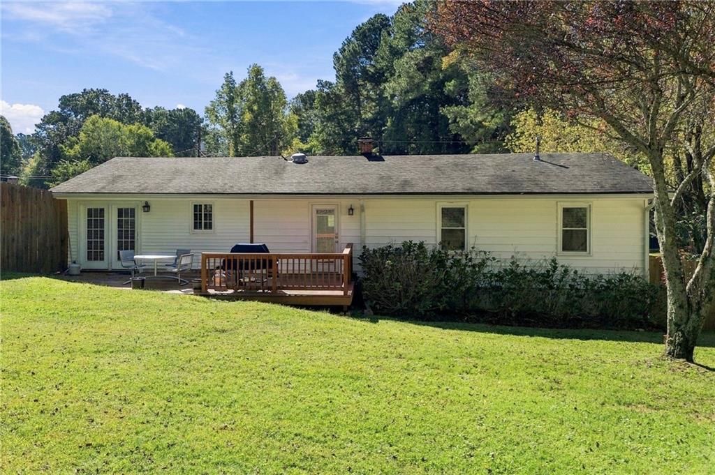 Rear of a single-story home with a wooden deck overlooking a broad lawn.